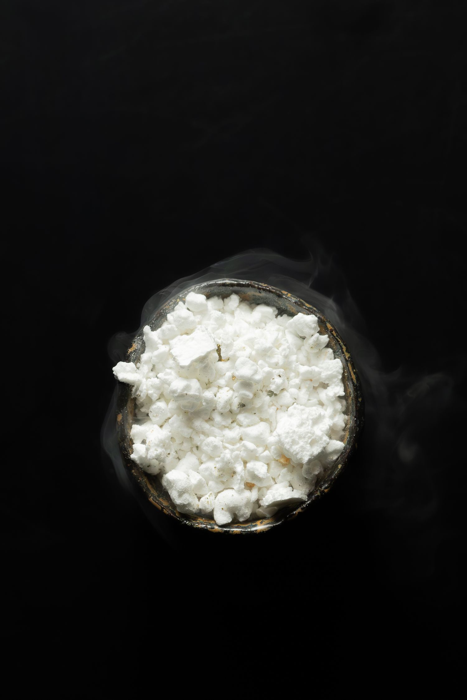 Overhead view of steaming white rice in a dark bowl against black background.