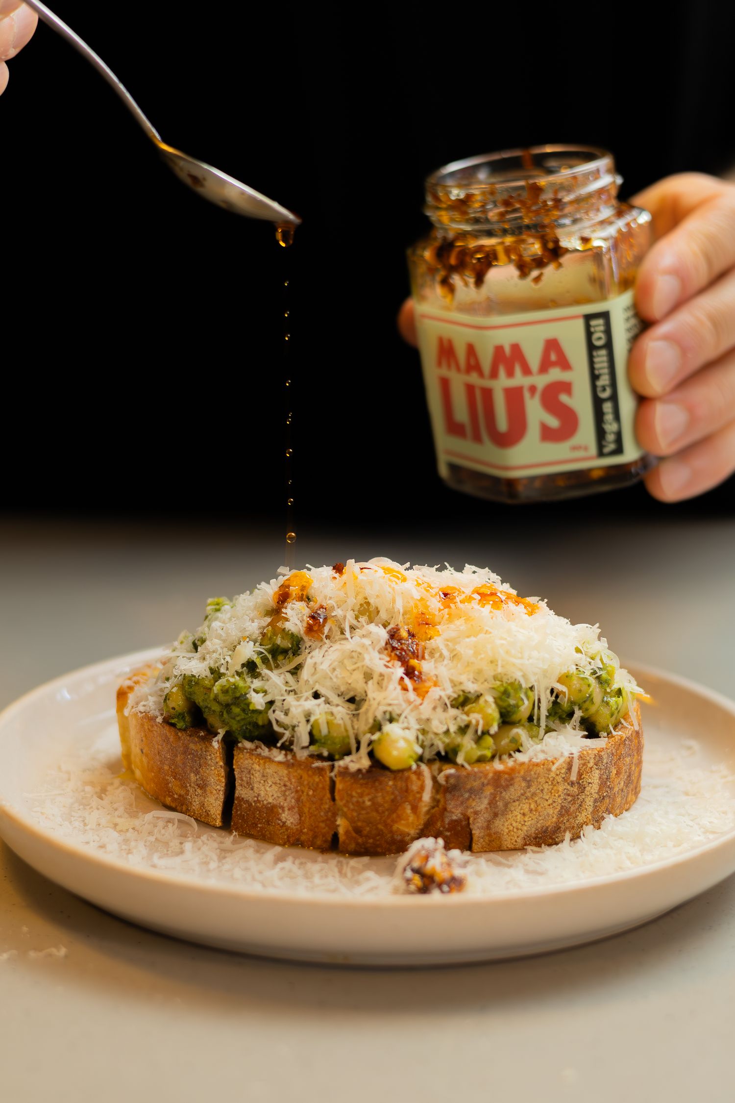 Artisanal toast topped with mashed avocado, cheese and a drizzle of Alma Liu's sauce on a white plate.