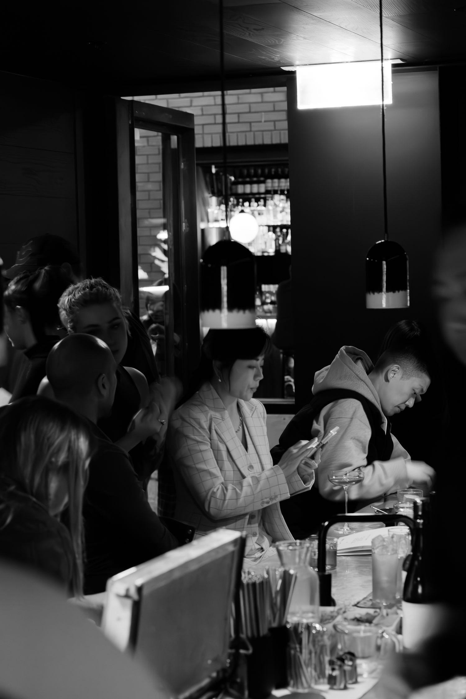 Black and white photo of a busy bar with patrons and bartenders mixing drinks in a dimly lit space.