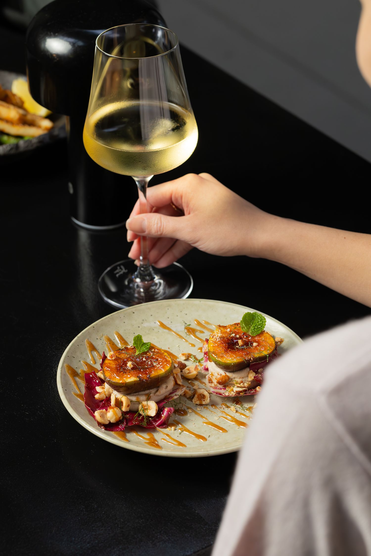 Elegant plated dish served with white wine in stemware on dark table.
