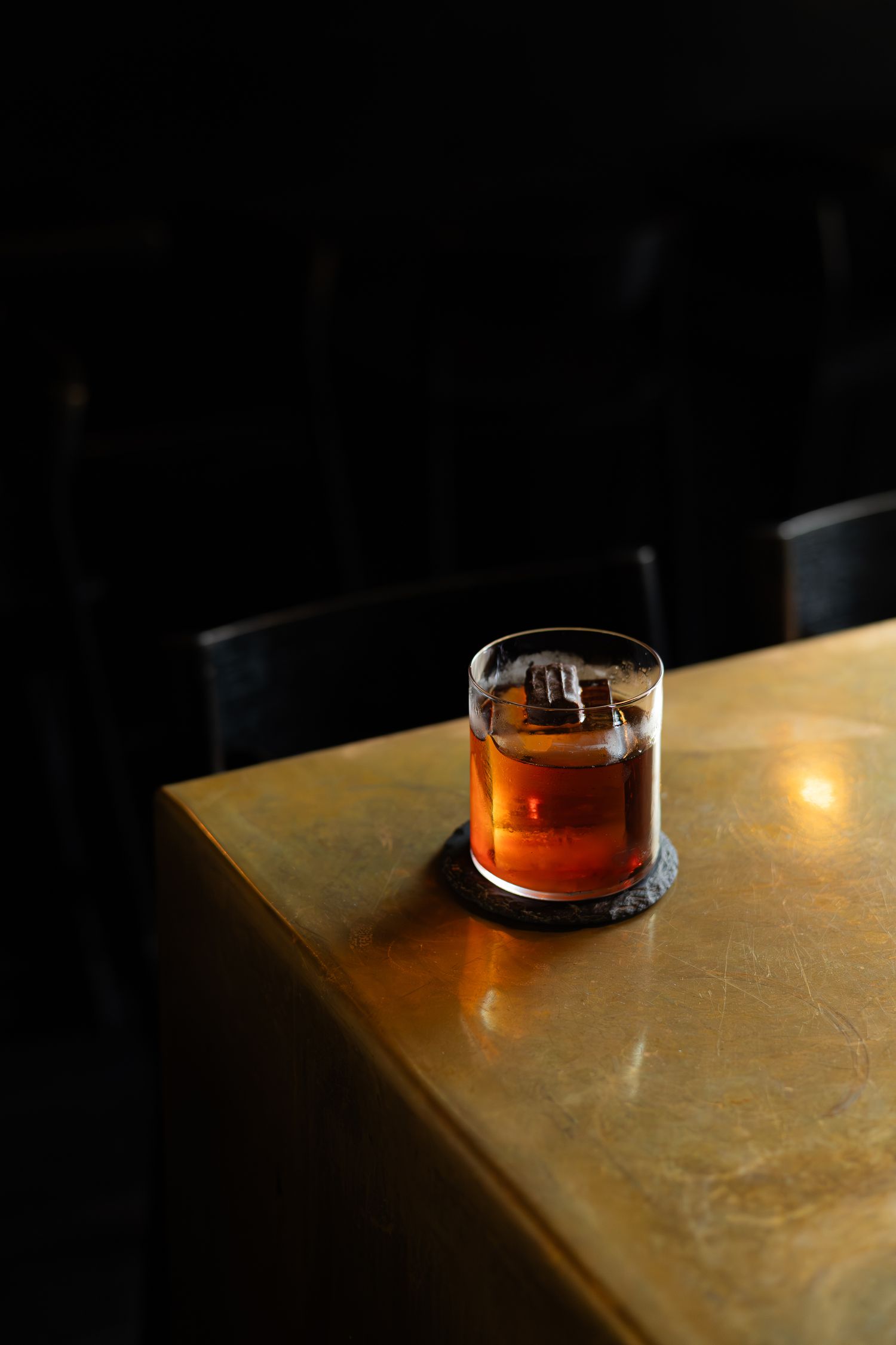 Amber colored cocktail with ice cube in lowball glass on wooden table.
