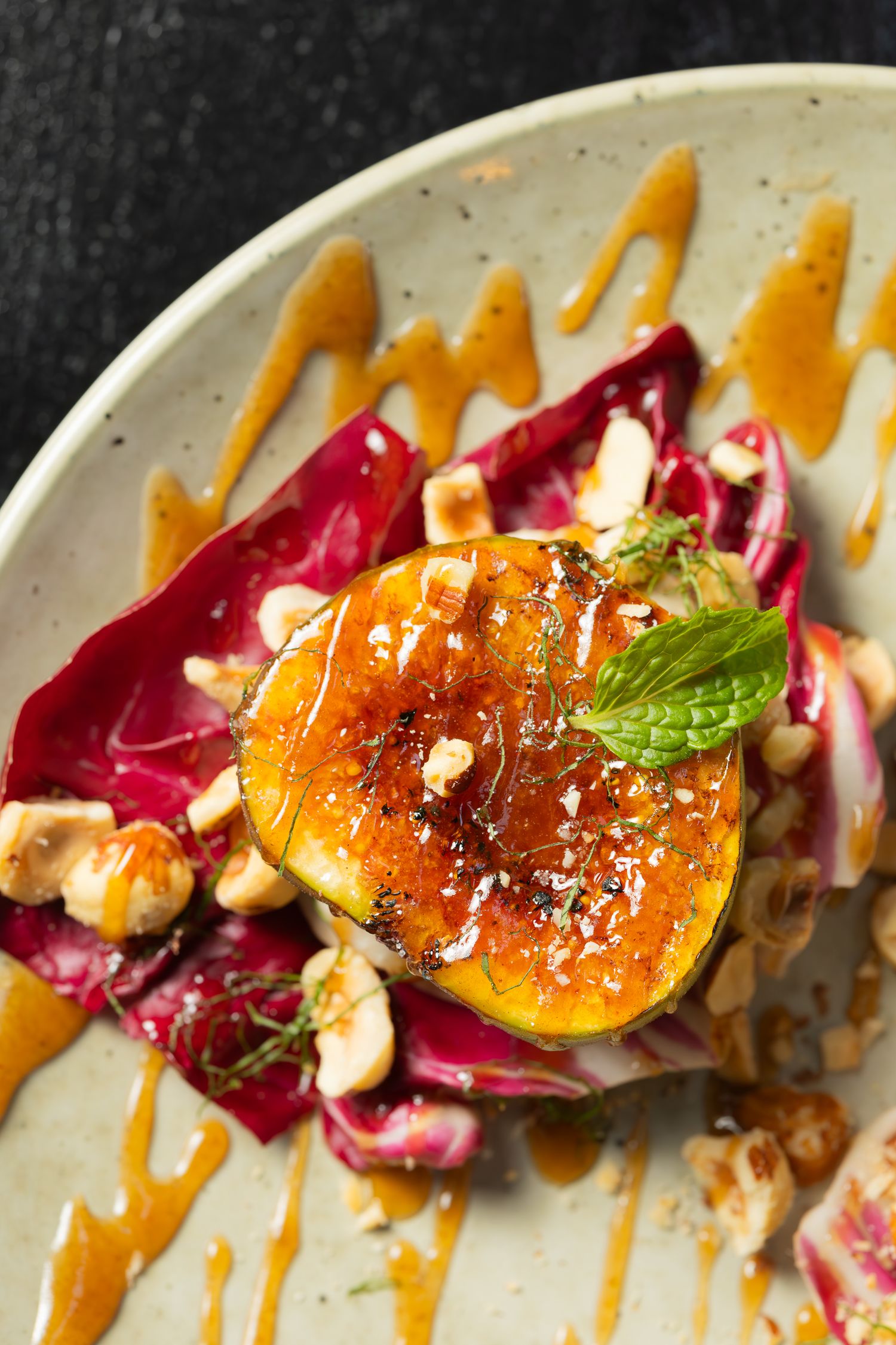 Grilled peach dish with radicchio, sauce drizzle, and fresh herbs on white plate.
