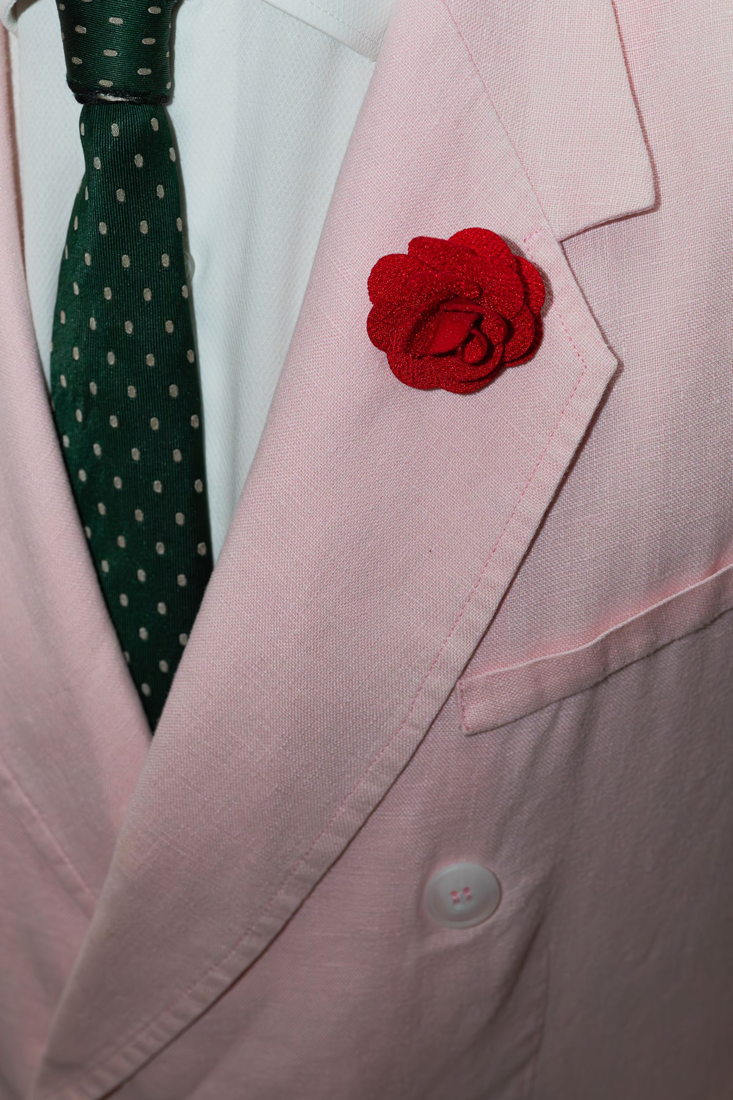 Close up detail of a pink suit jacket with green polka dot tie and red flower lapel pin.