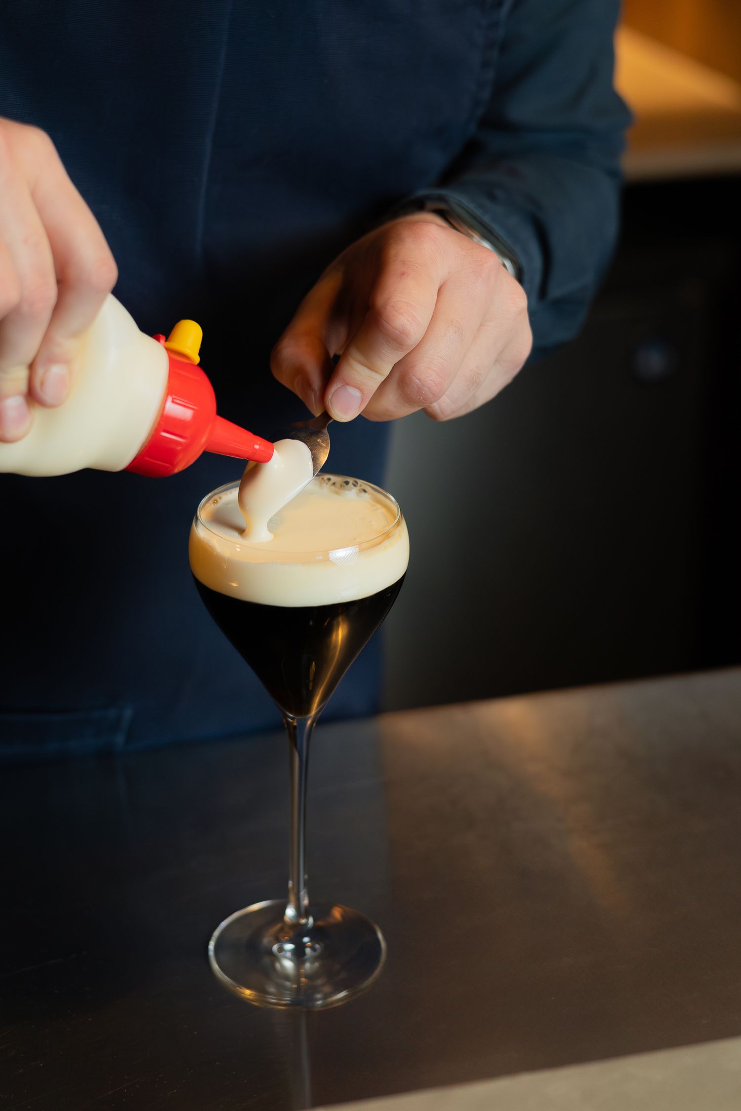 Bartender adding cream topping to an espresso cocktail in stemmed glass.