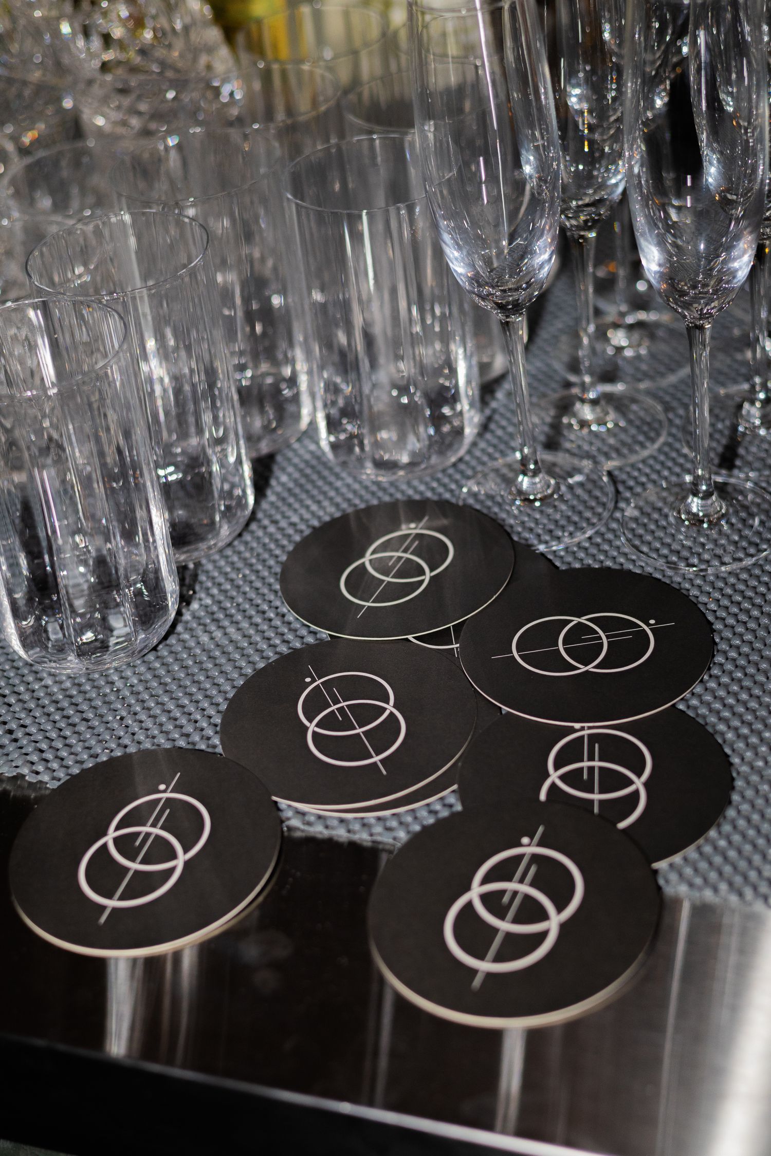 Empty champagne flutes arranged on bar mat with black branded coasters displaying interlocking circles.