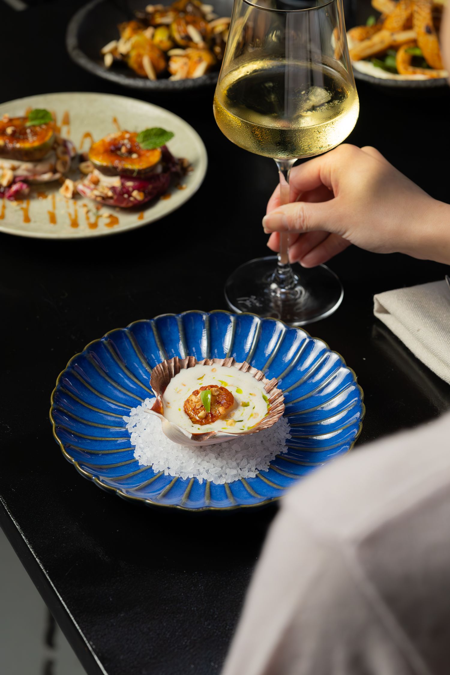 A sophisticated dining scene with a white wine glass and fresh oyster on a decorative blue plate.