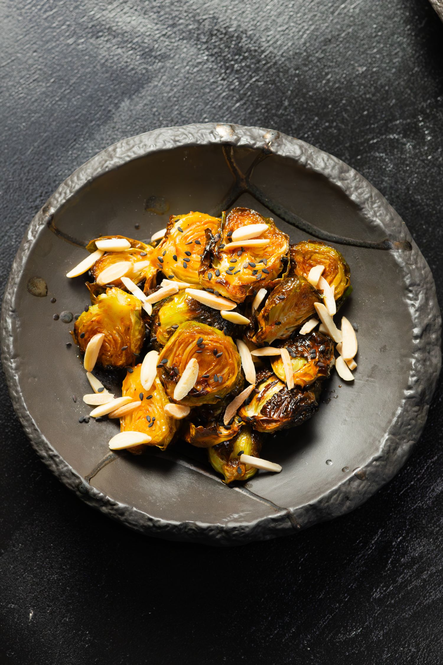 Roasted brussels sprouts with shaved parmesan cheese on dark ceramic plate.