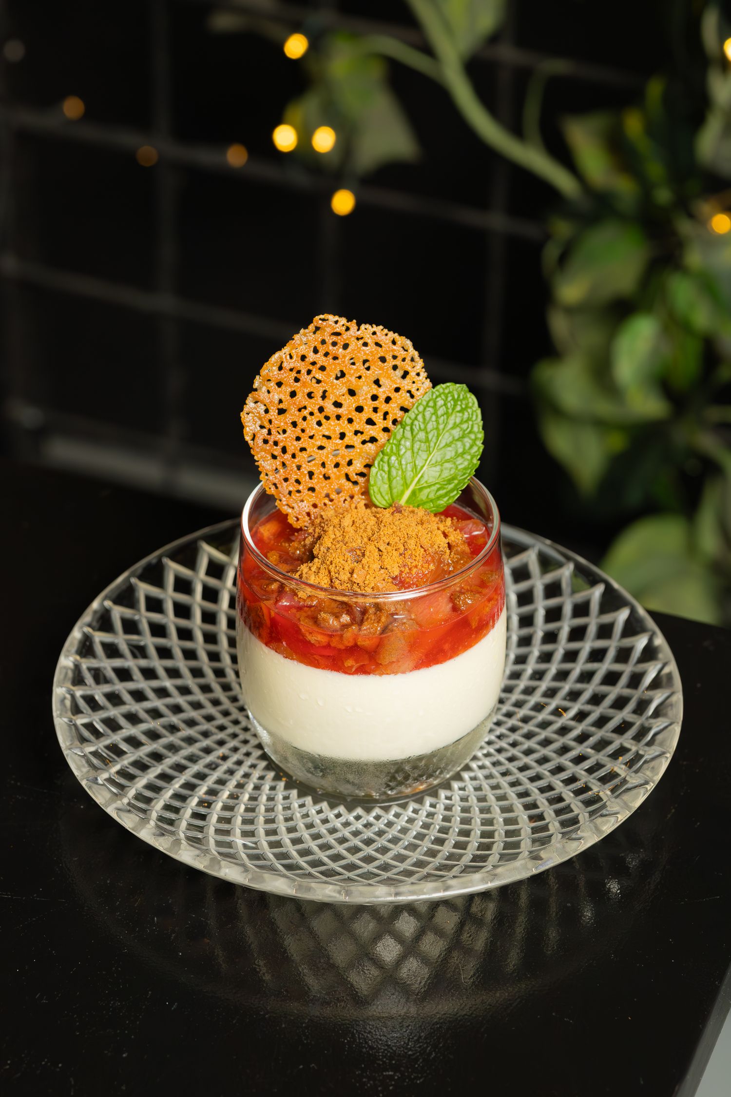Layered dessert with white cream and red topping garnished with lace cookie and mint.