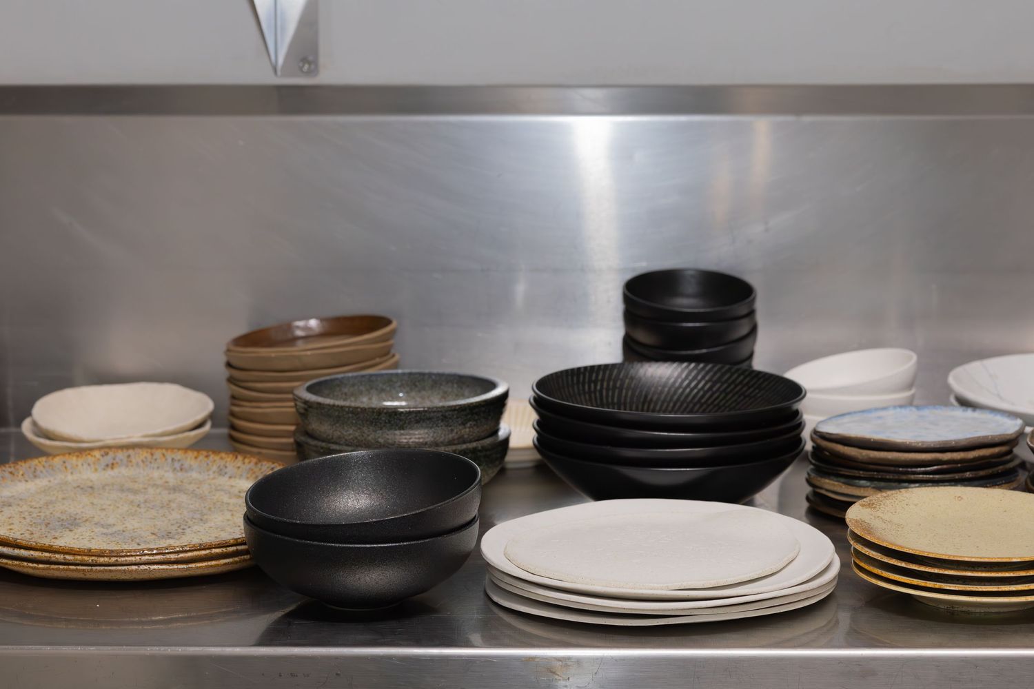 Collection of stacked ceramic plates in black, white and neutral tones on metal shelving.