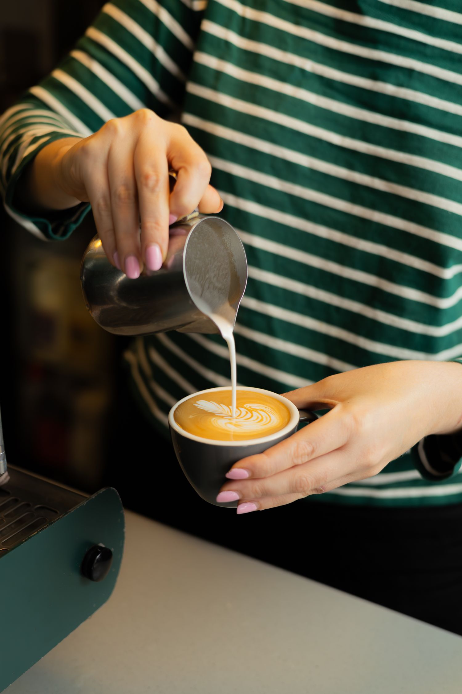 Barista pouring steamed milk into coffee cup creating latte art pattern.