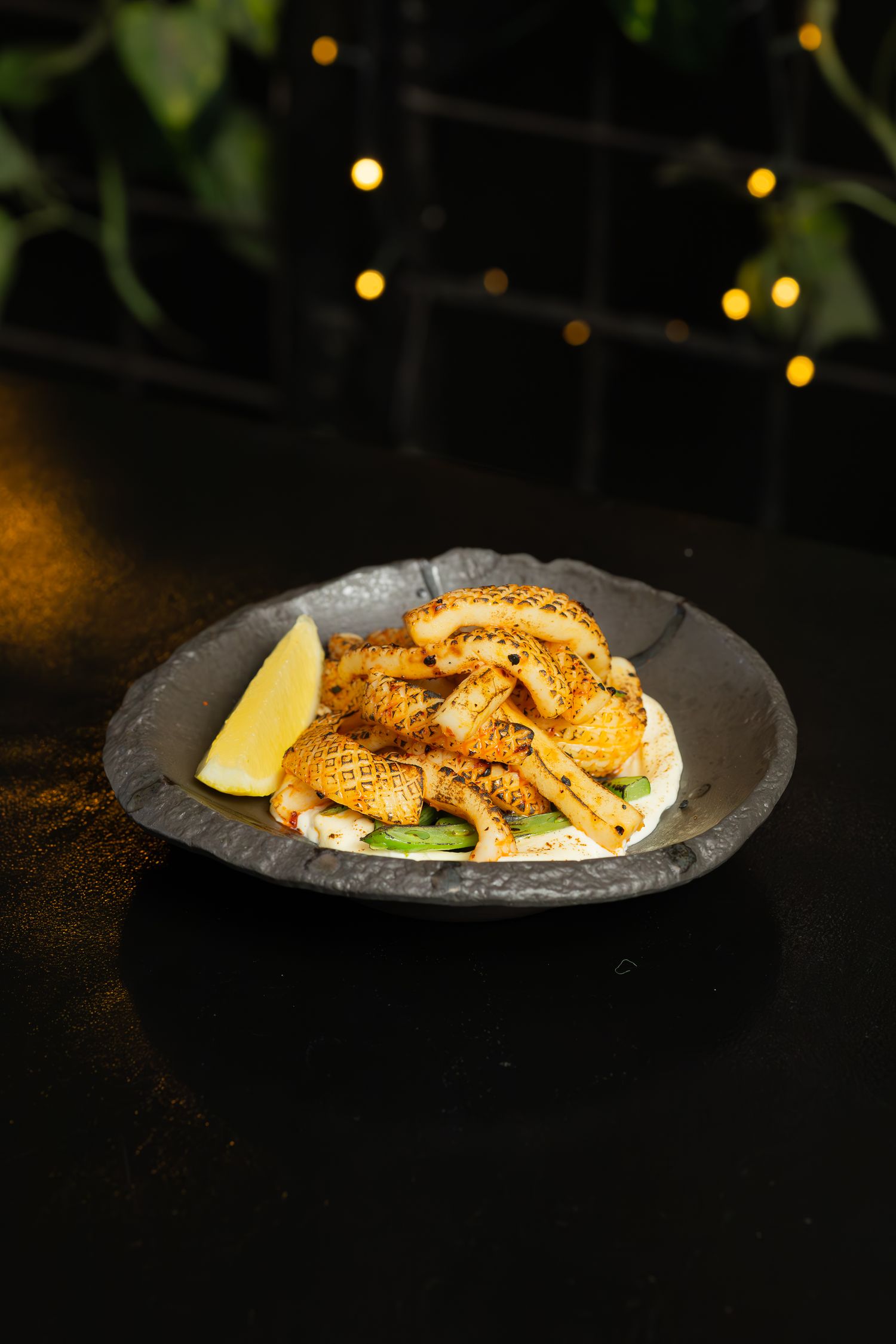 Crispy topped fish dish served on a dark plate with lemon wedge and garnish.