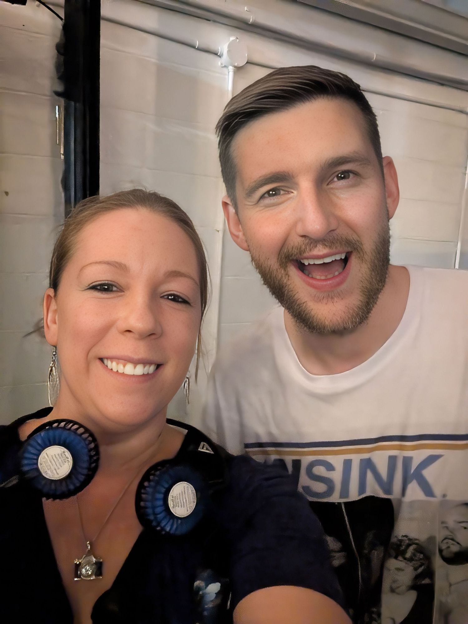 Jeremiah Watkins comedian. Two smiling people pose for a selfie, woman wearing blue rosette earrings and man in white graphic tee.