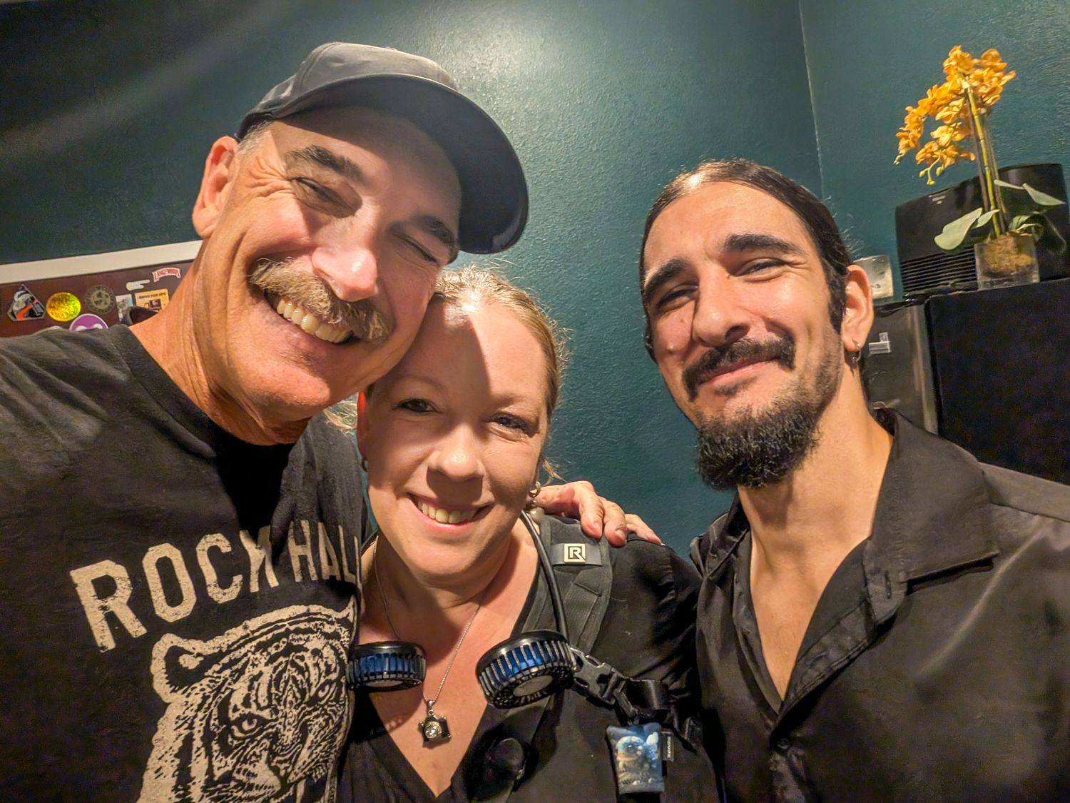 Three friends smiling together in a selfie, man in Rock Hall cap, woman in black, bearded man on right.