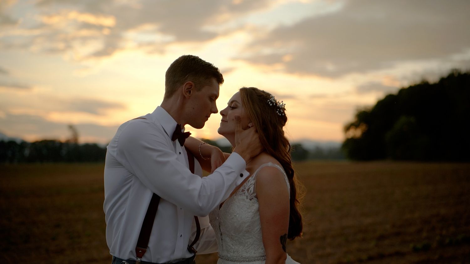 A couple shares a romantic moment at sunset in an open field with golden light illuminating the scene.