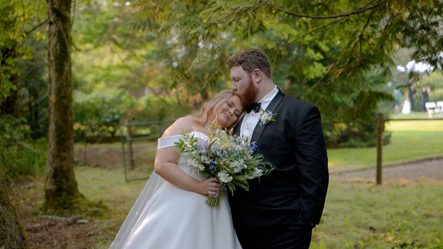 A romantic moment between newlyweds holding a white and green floral bouquet in a tranquil garden setting.