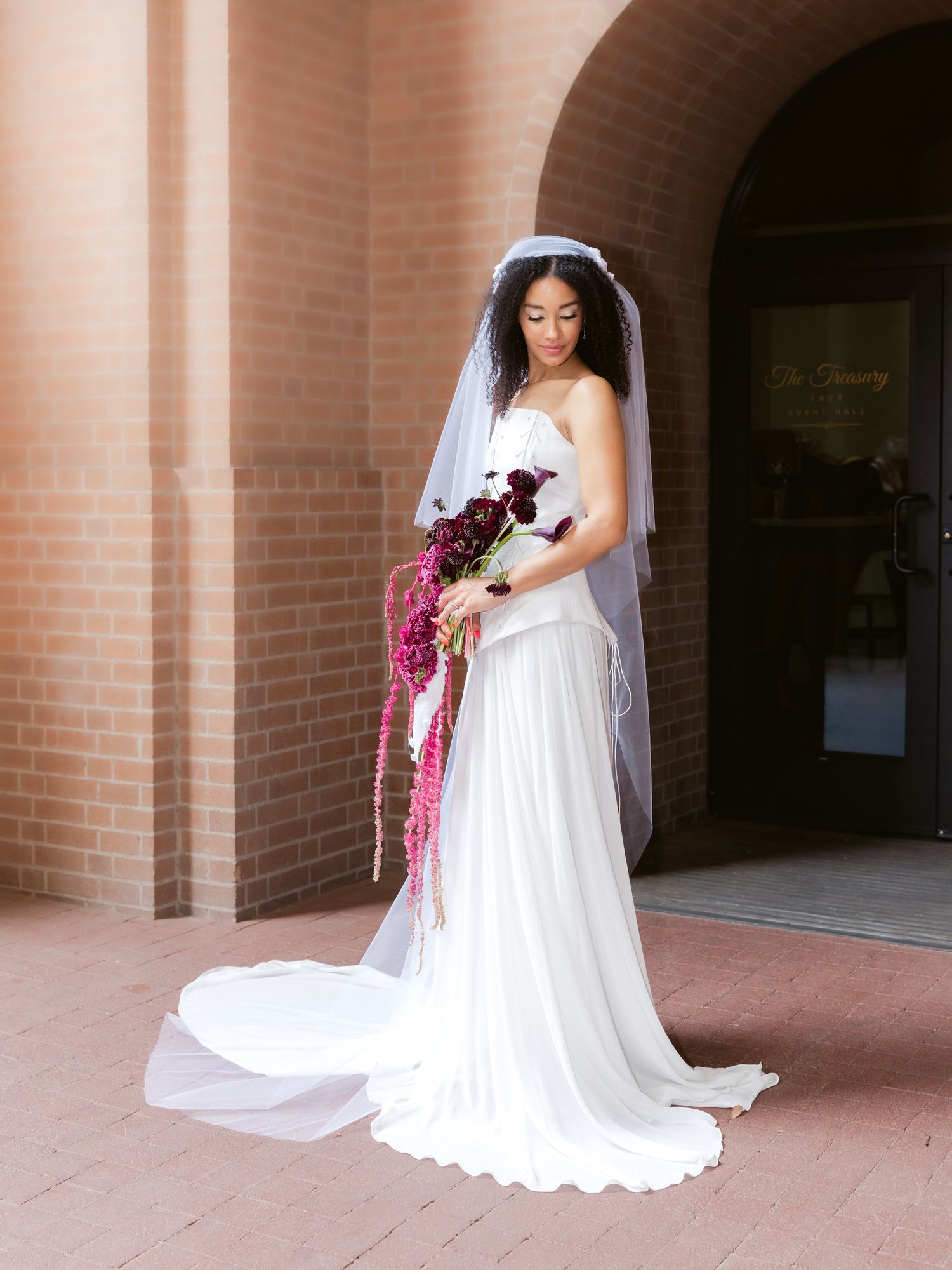 Elegant bride in white gown with cathedral veil holds cascading burgundy bridal bouquet.