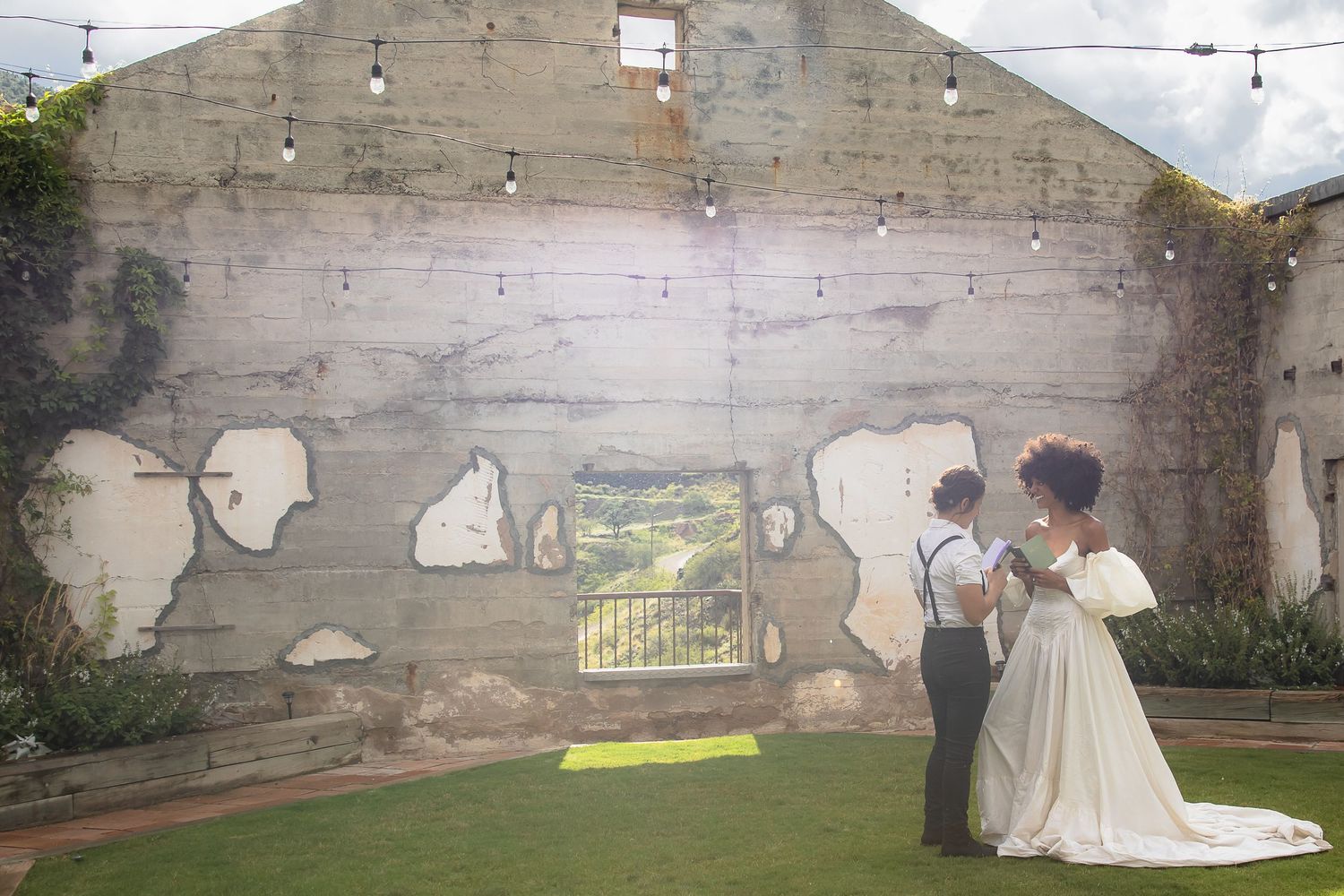 Bride and groom share a romantic moment before a rustic wall with string lights.
