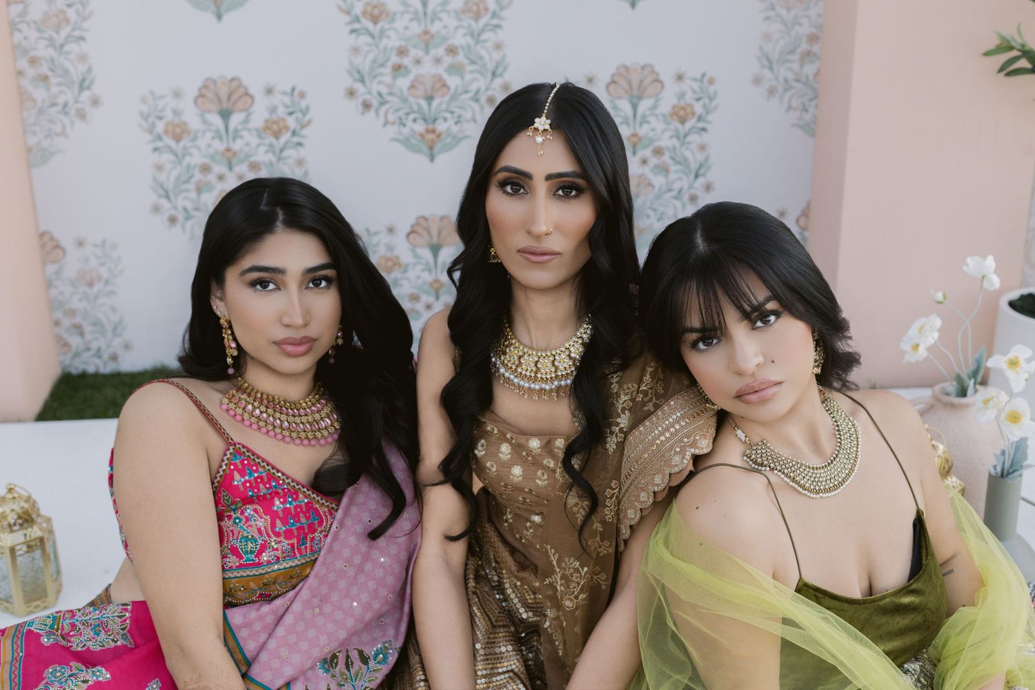 Three women in elegant Indian attire pose together at a festive celebration.