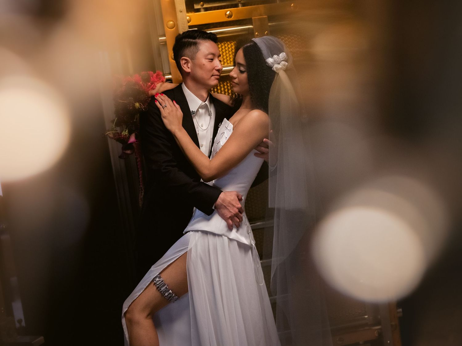 Bride and groom share romantic embrace in dimly lit venue, bride wearing strapless gown and veil.