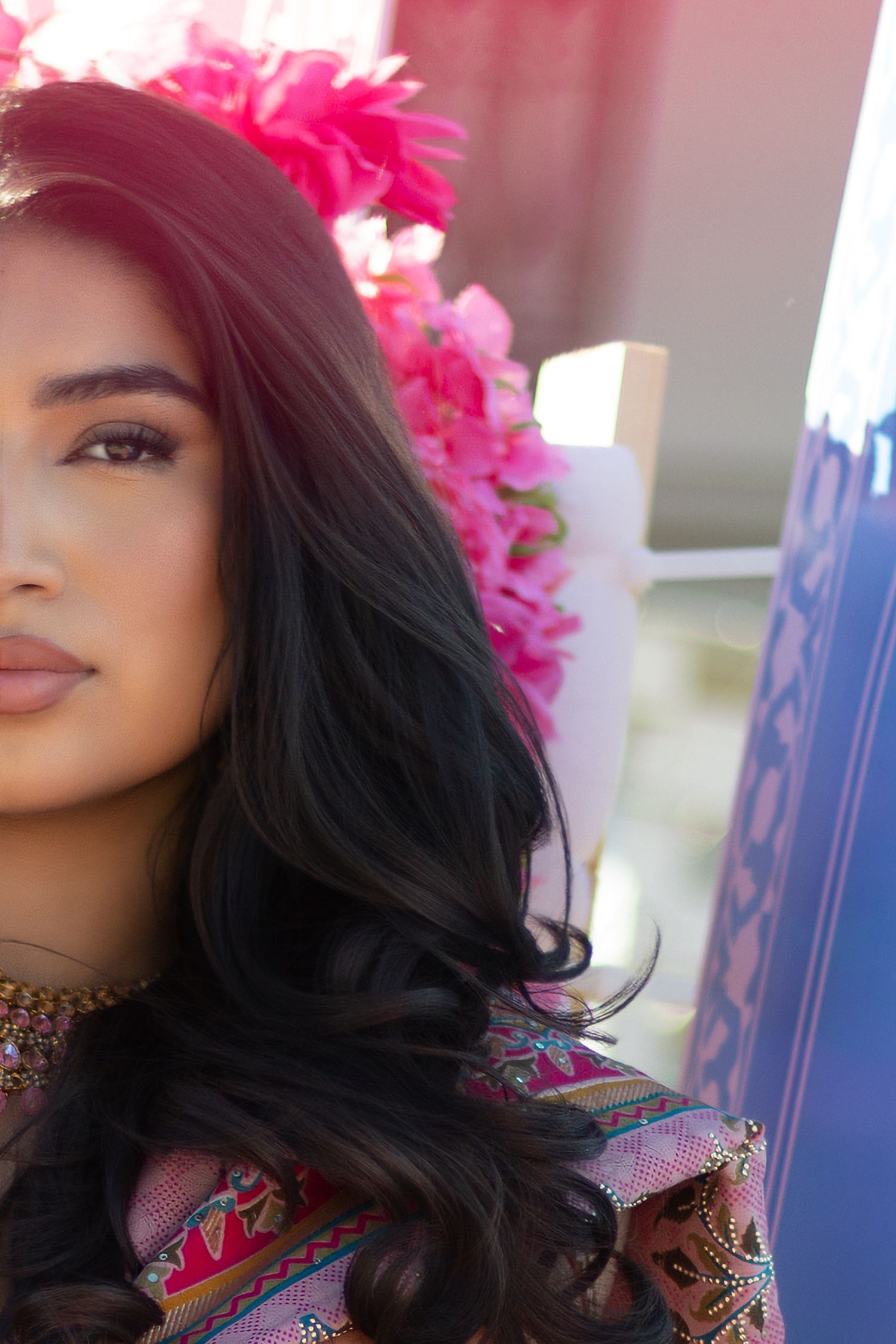 Close-up portrait of a woman with long dark hair adorned with vibrant pink flowers.