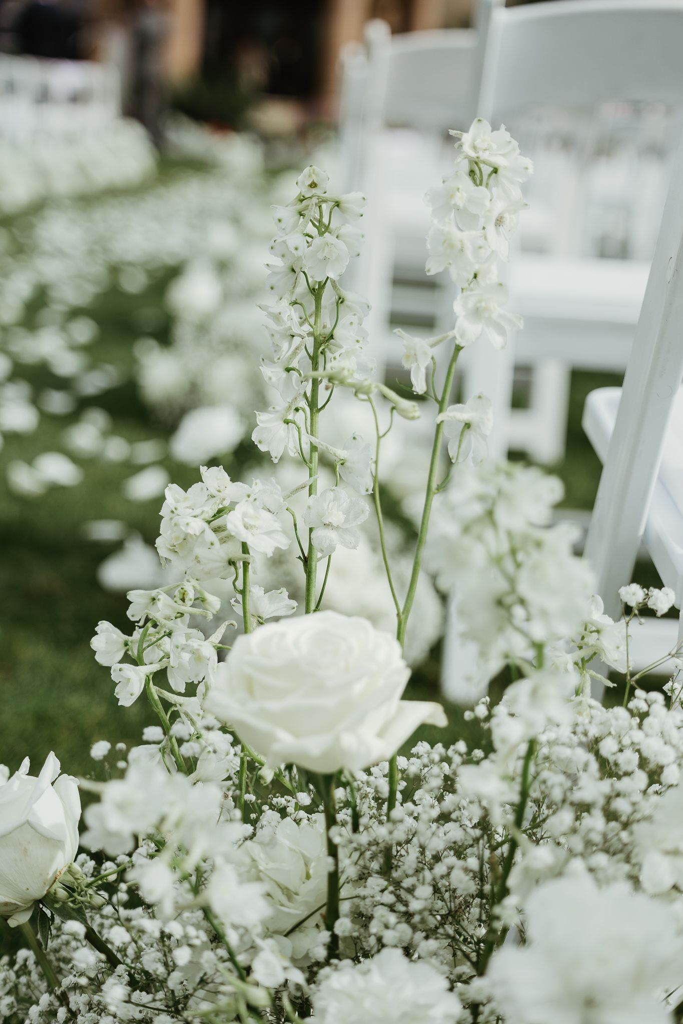Elegant white roses and baby's breath floral arrangements lining a wedding ceremony aisle.