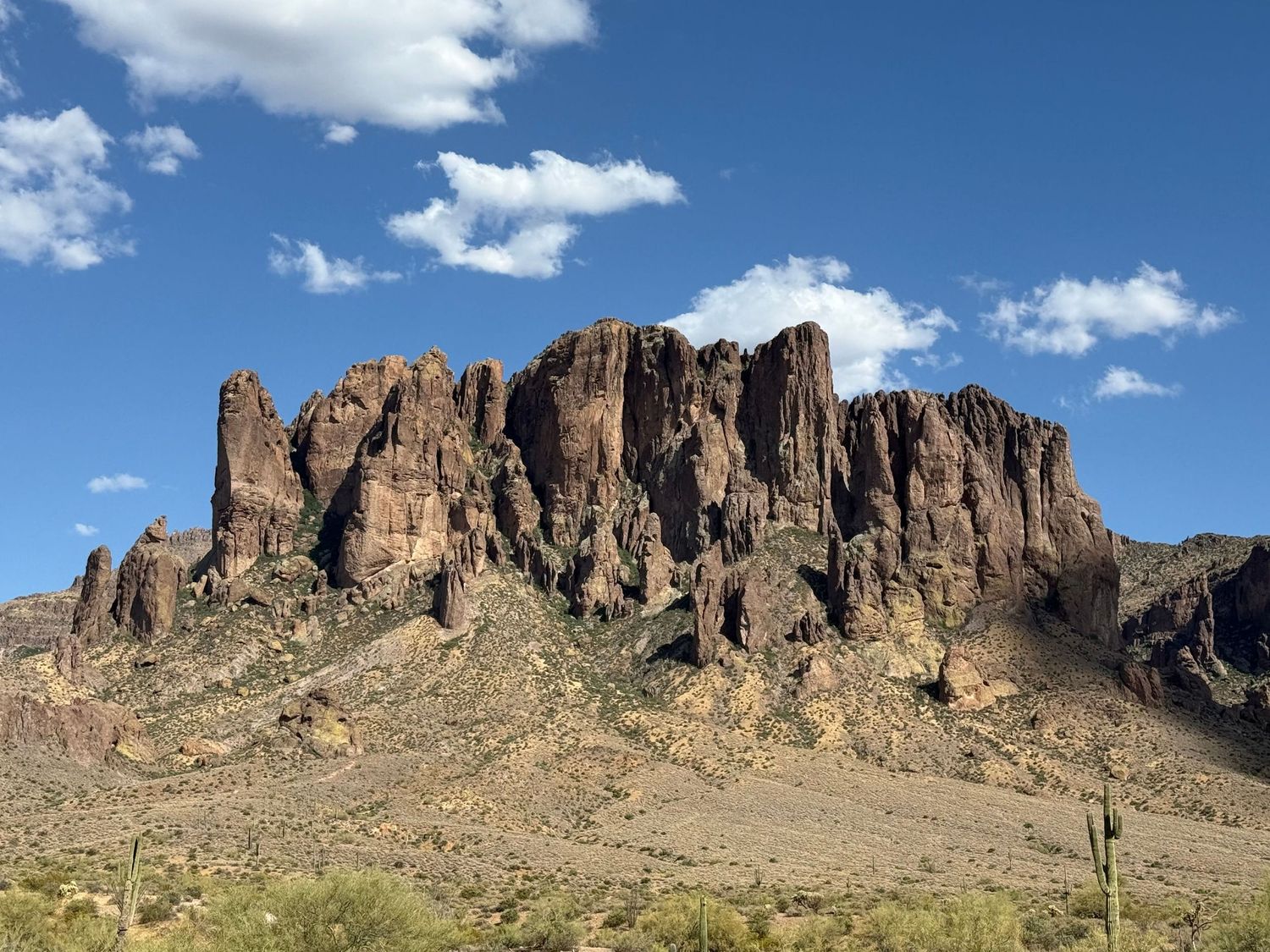 Rugged red rock Superstition Mountains rise dramatically against a blue sky with white clouds in the Arizona desert.