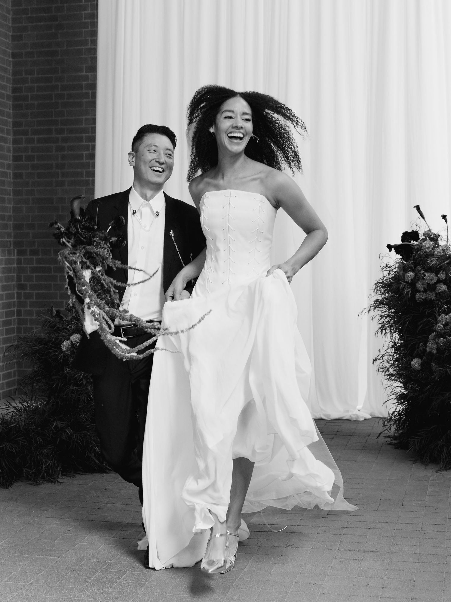 Joyful bride in strapless white gown laughs with groom during wedding reception entrance.