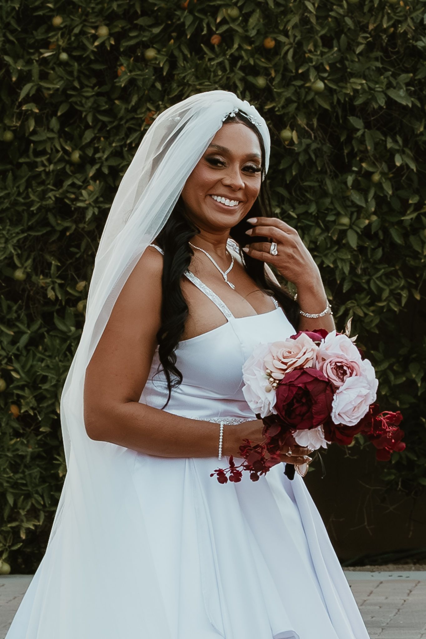 Radiant Black bride in white gown and veil holding pink and red rose bouquet outdoors.