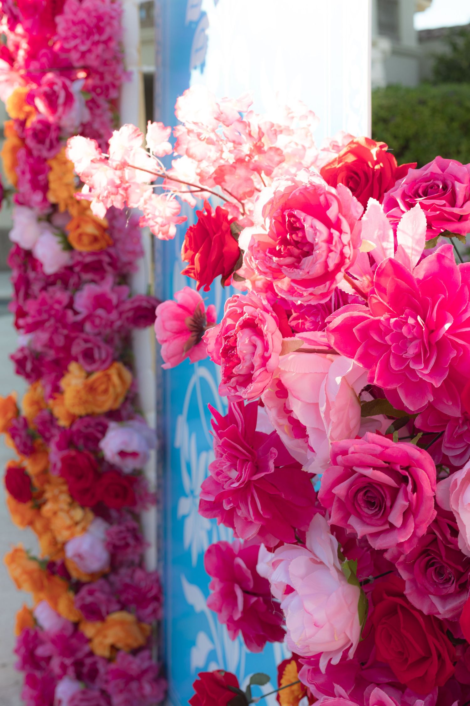 Colorful pink and orange flower wall decoration with roses and garlands at festive Indian wedding event.