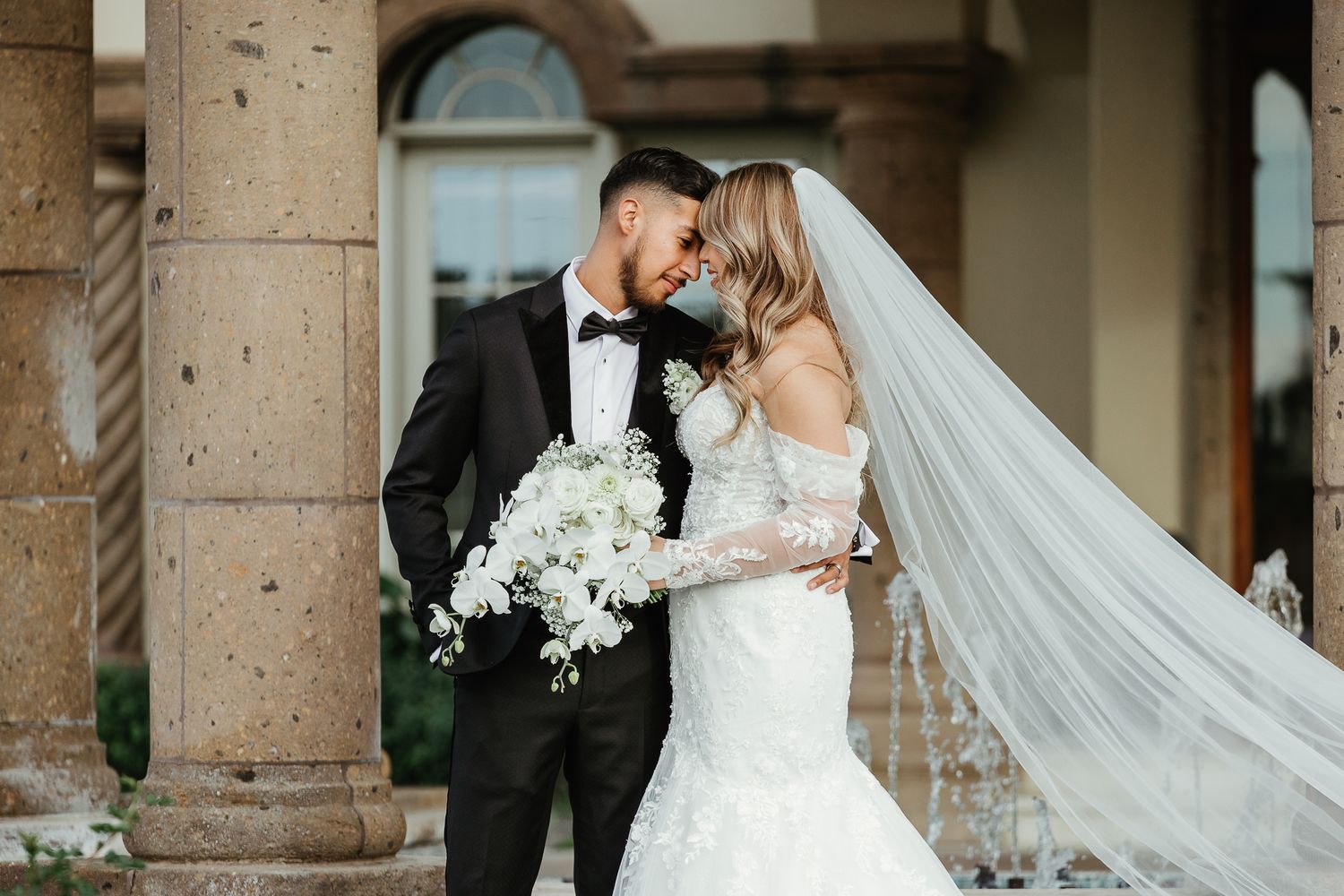 Bride and groom sharing romantic moment outdoors, bride in lace gown with flowing veil.