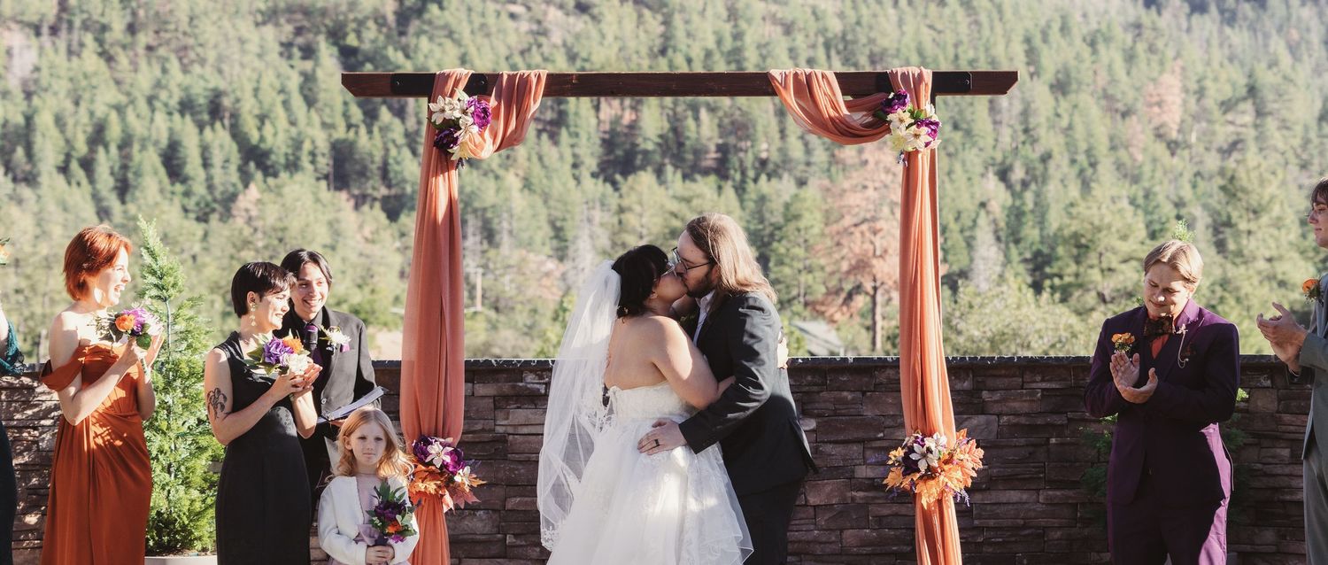 Bride and groom share a kiss under a rustic wooden arch with autumn decor.