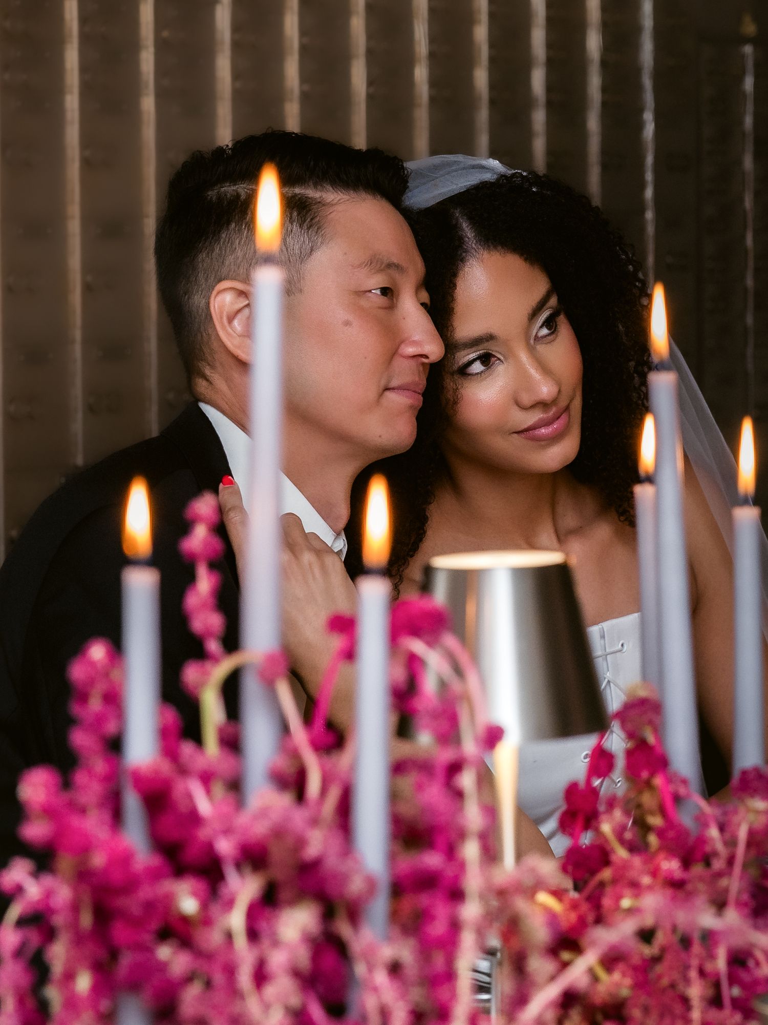 Bride and groom share intimate moment at candlelit table adorned with pink floral arrangements at wedding.