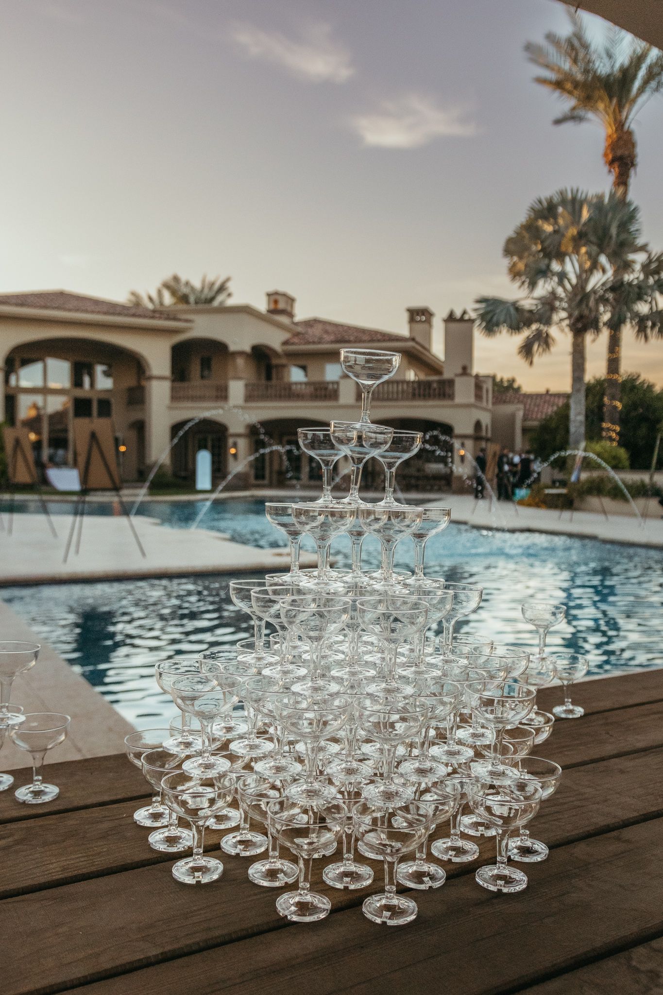 Elegant champagne tower pyramid displayed poolside at luxury wedding venue at sunset.
