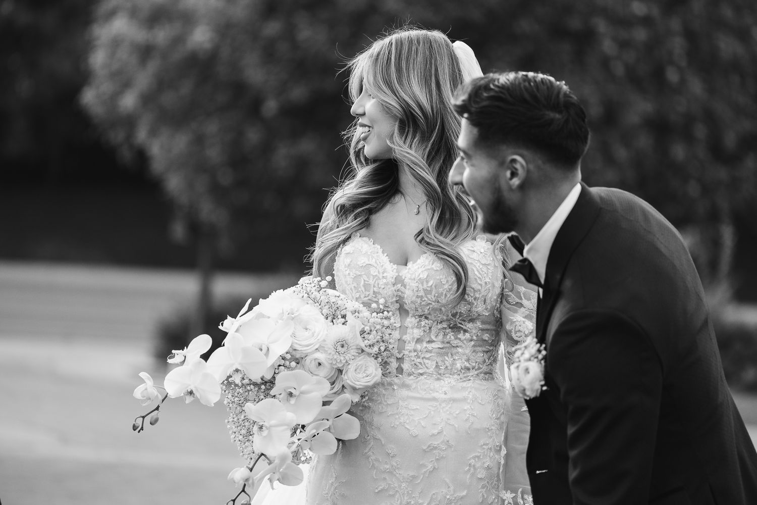 Black and white photo of laughing bride and groom sharing a joyful moment outdoors on their wedding day.