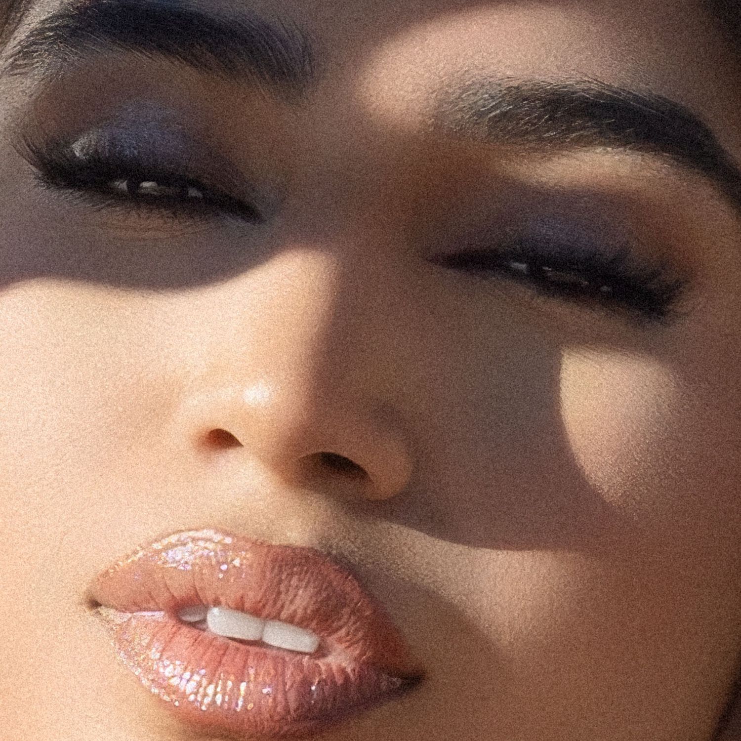 Close-up beauty shot of woman with dramatic smoky eye makeup and glossy nude lips in sunlight.