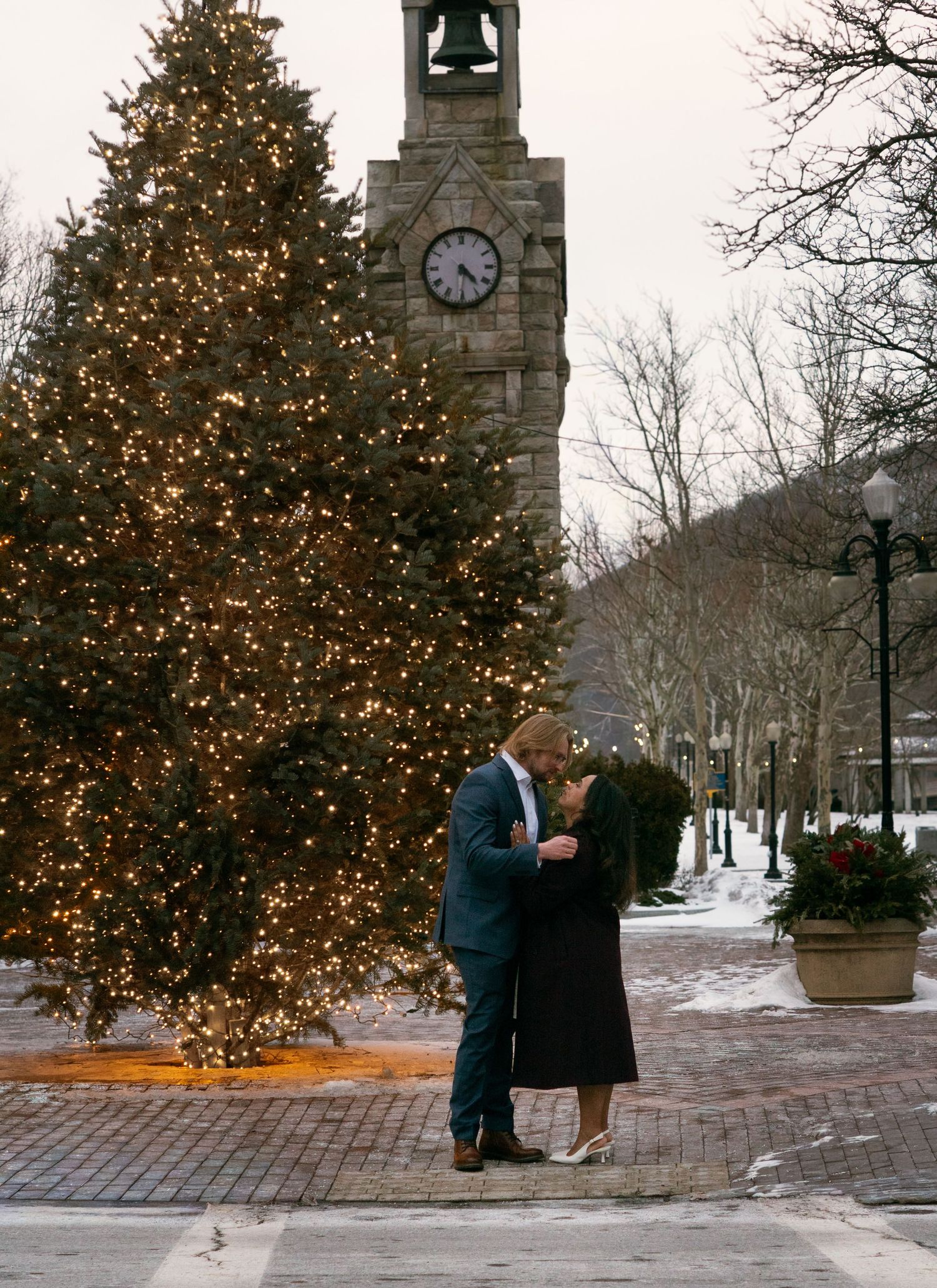 Couple standing in front of the Market Street clock and Holiday Christmas tree in Corning, NY during a winter wedding engagement session