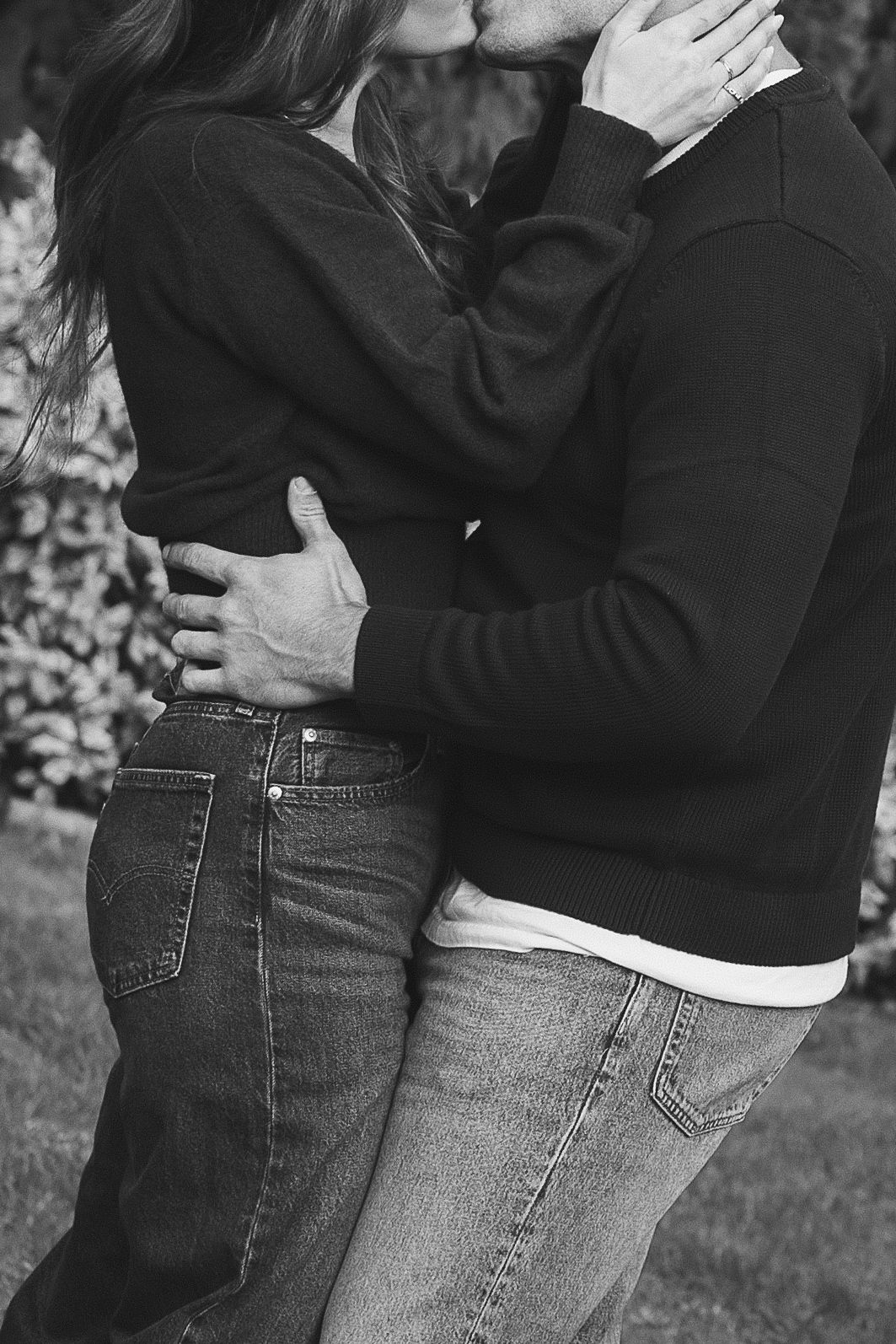 Black and white photo of a couple kissing and embracing outdoors in a garden setting.