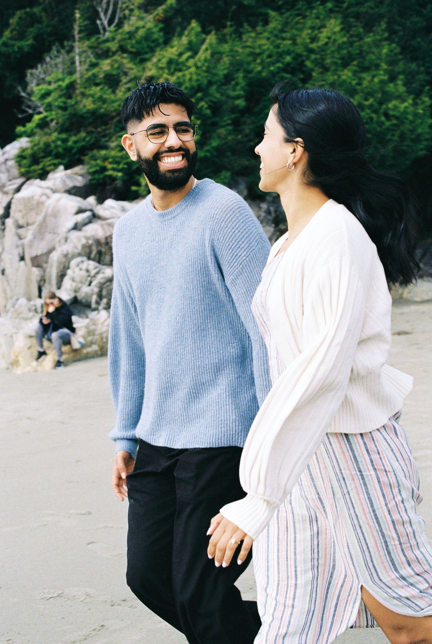 Happy bearded man smiling at woman while walking hand in hand on a sandy beach.