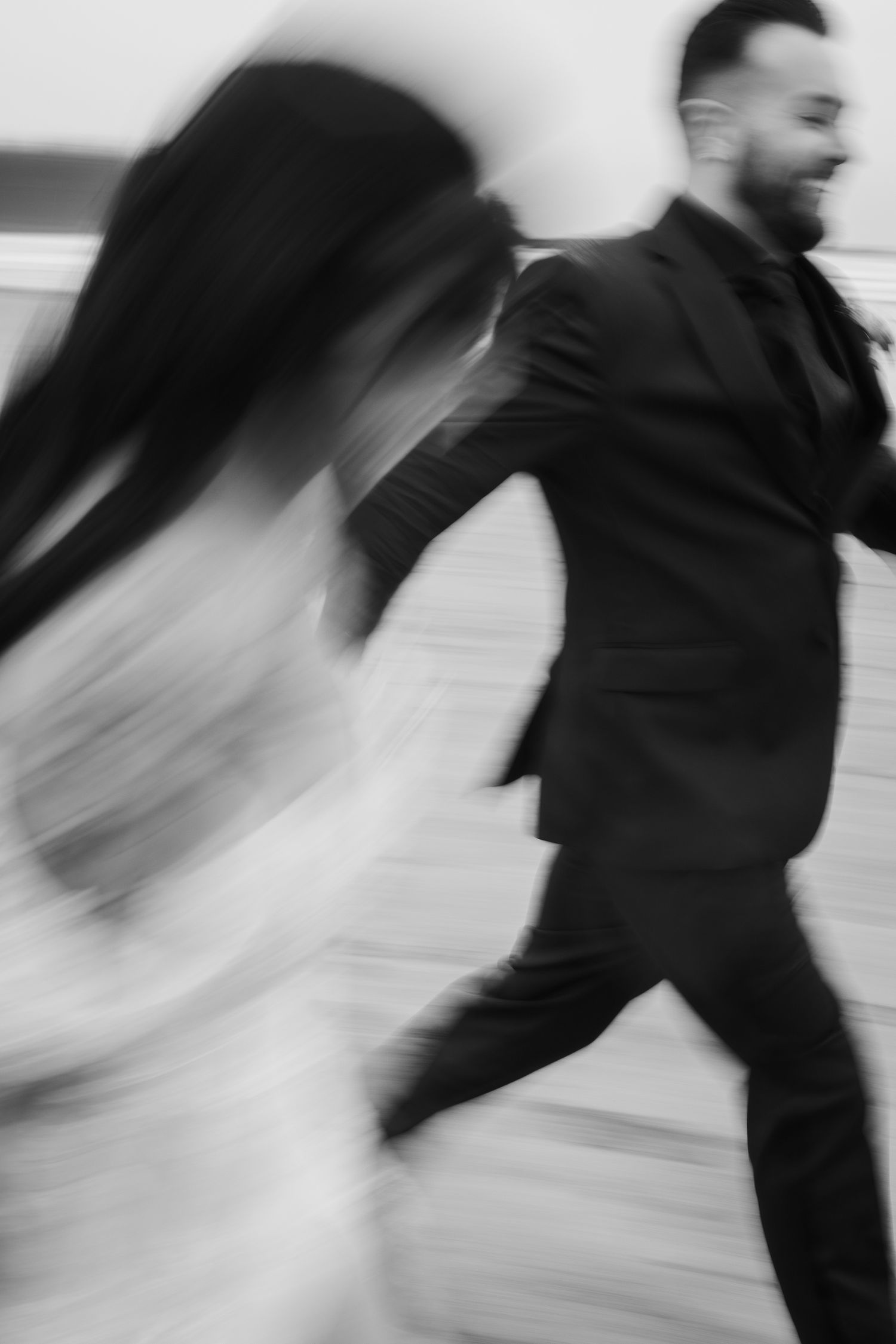 Artistic blurred black and white photo of bride and groom running together on their wedding day.