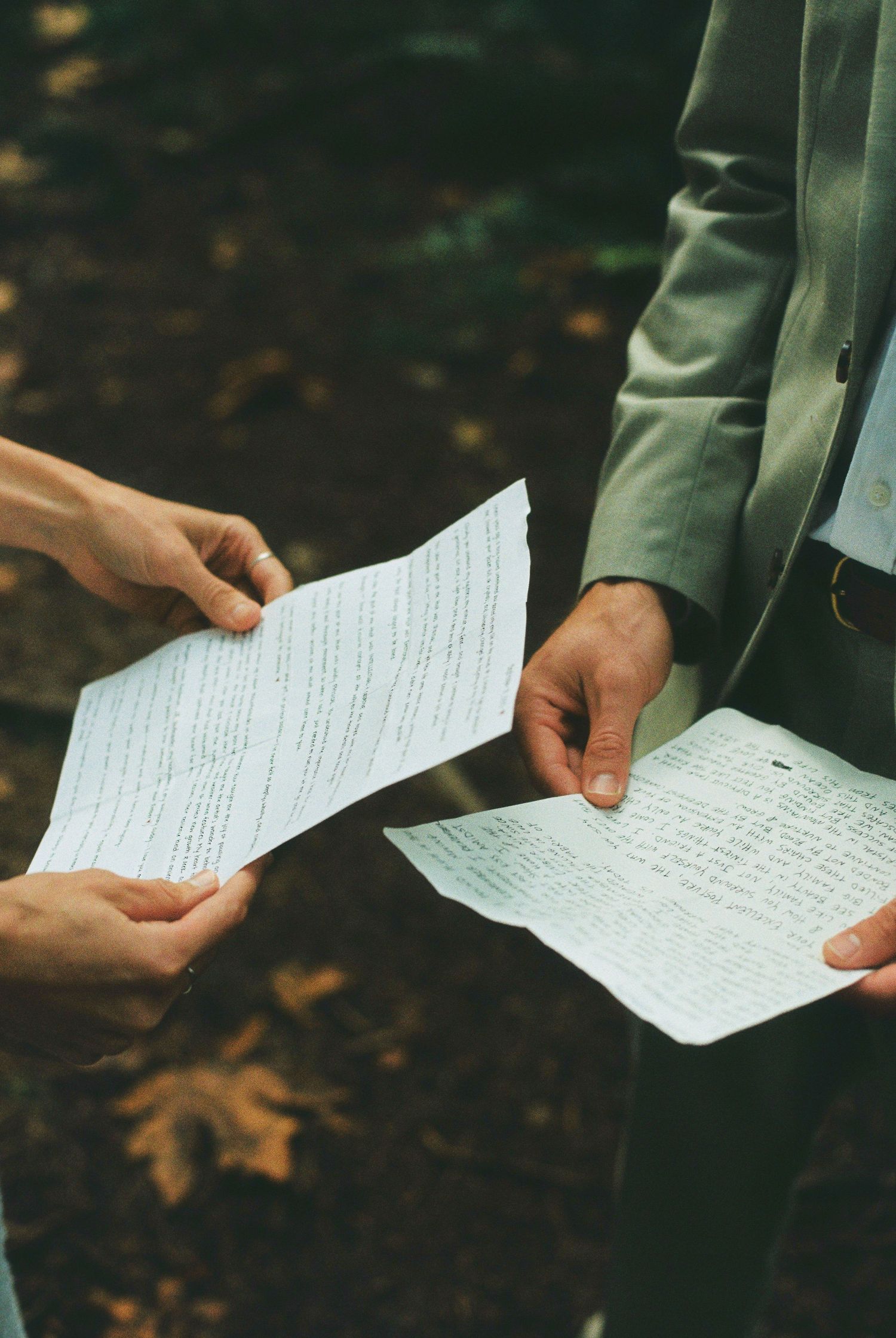 Bride and groom exchange handwritten wedding vows outdoors, holding papers with autumn leaves in background.