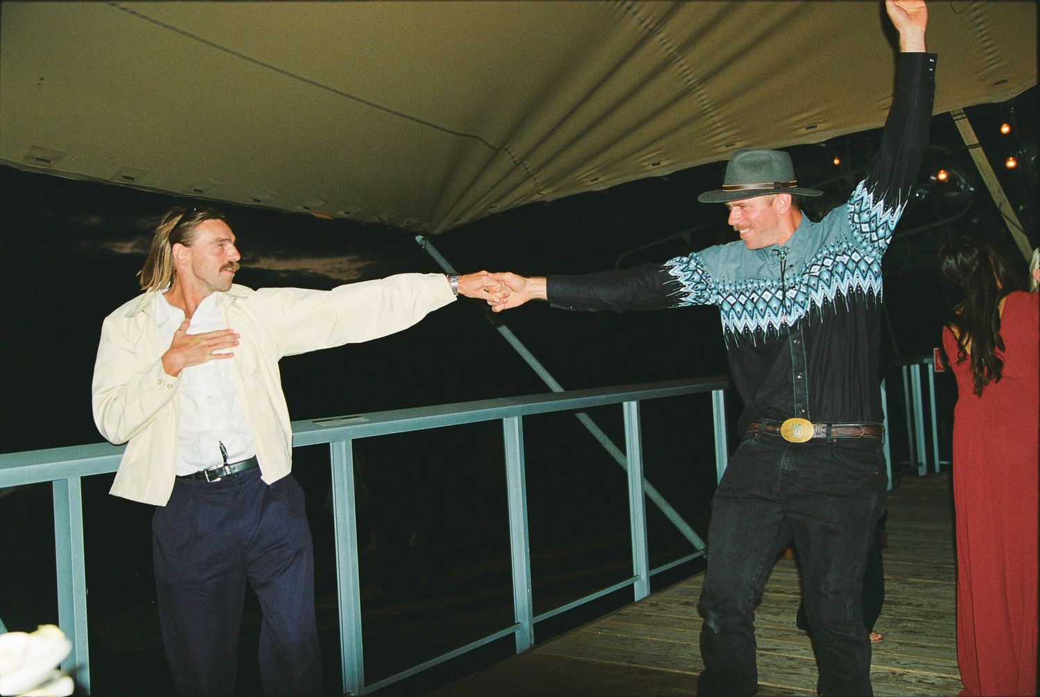 Two wedding guests joyfully dancing together on outdoor deck at night.