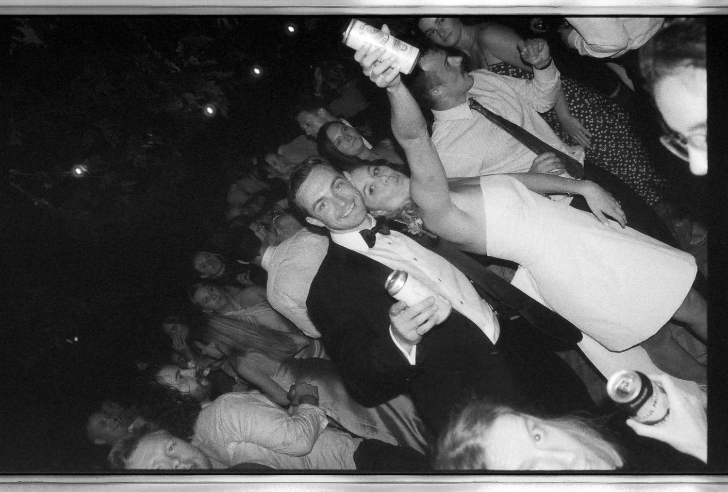 Black and white candid photo of wedding guests dancing and celebrating at a lively outdoor reception.