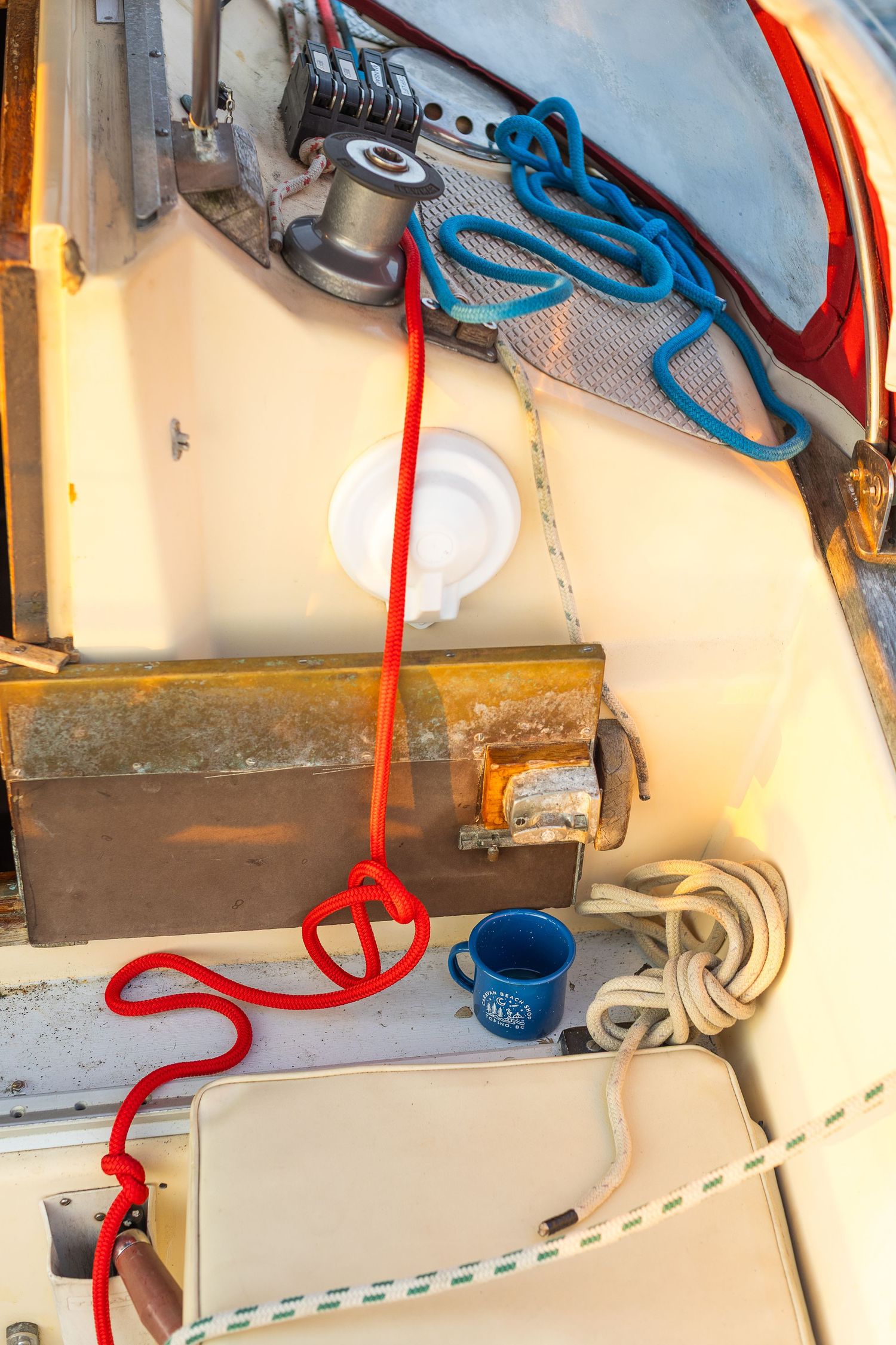 Overhead view of sailboat deck with red and blue ropes, metal box, and blue enamel mug.