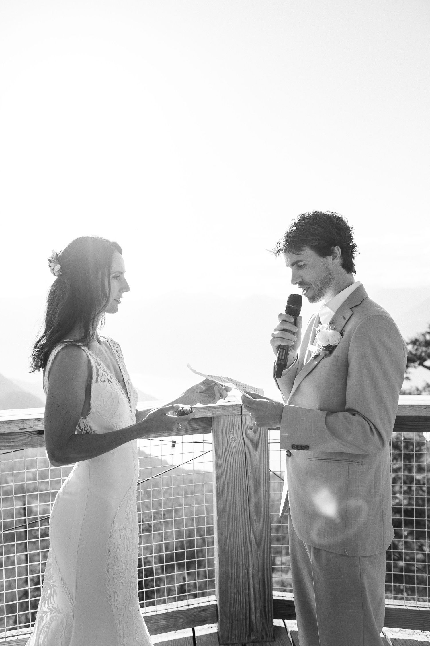 Black and white photo of groom reading vows to bride at outdoor mountain wedding ceremony.