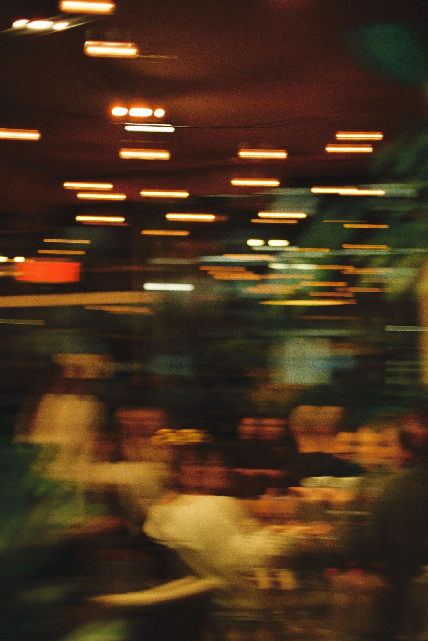 Motion blur artistic photo of busy restaurant interior with warm overhead lights and dining guests.