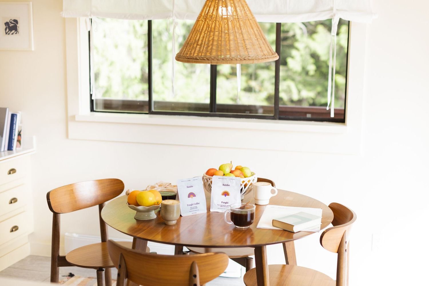 Cozy dining table with fruit bowl, coffee mug, and Pangia Coffee packet under wicker pendant light.