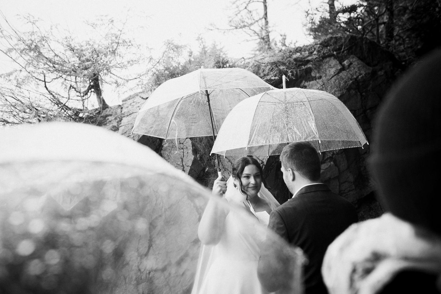 Black and white photo of emotional bride during rainy outdoor wedding ceremony with umbrellas.