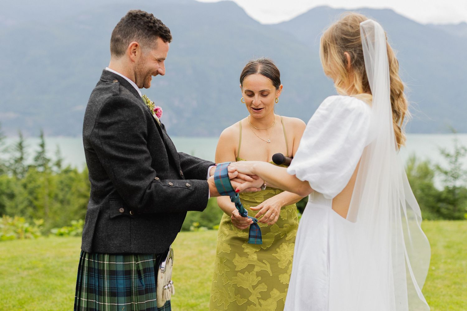 Bride and groom exchanging rings during outdoor wedding ceremony with mountain lake views in background.