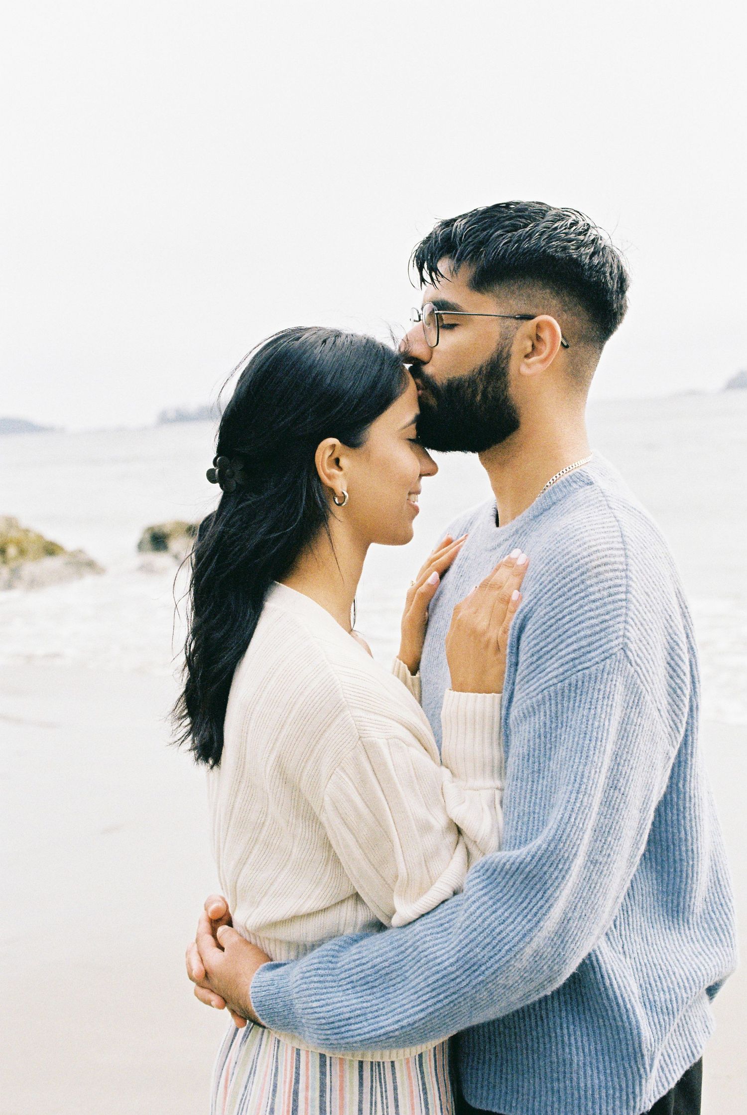 Couple embracing intimately on a beach, woman placing hands on mans chest.