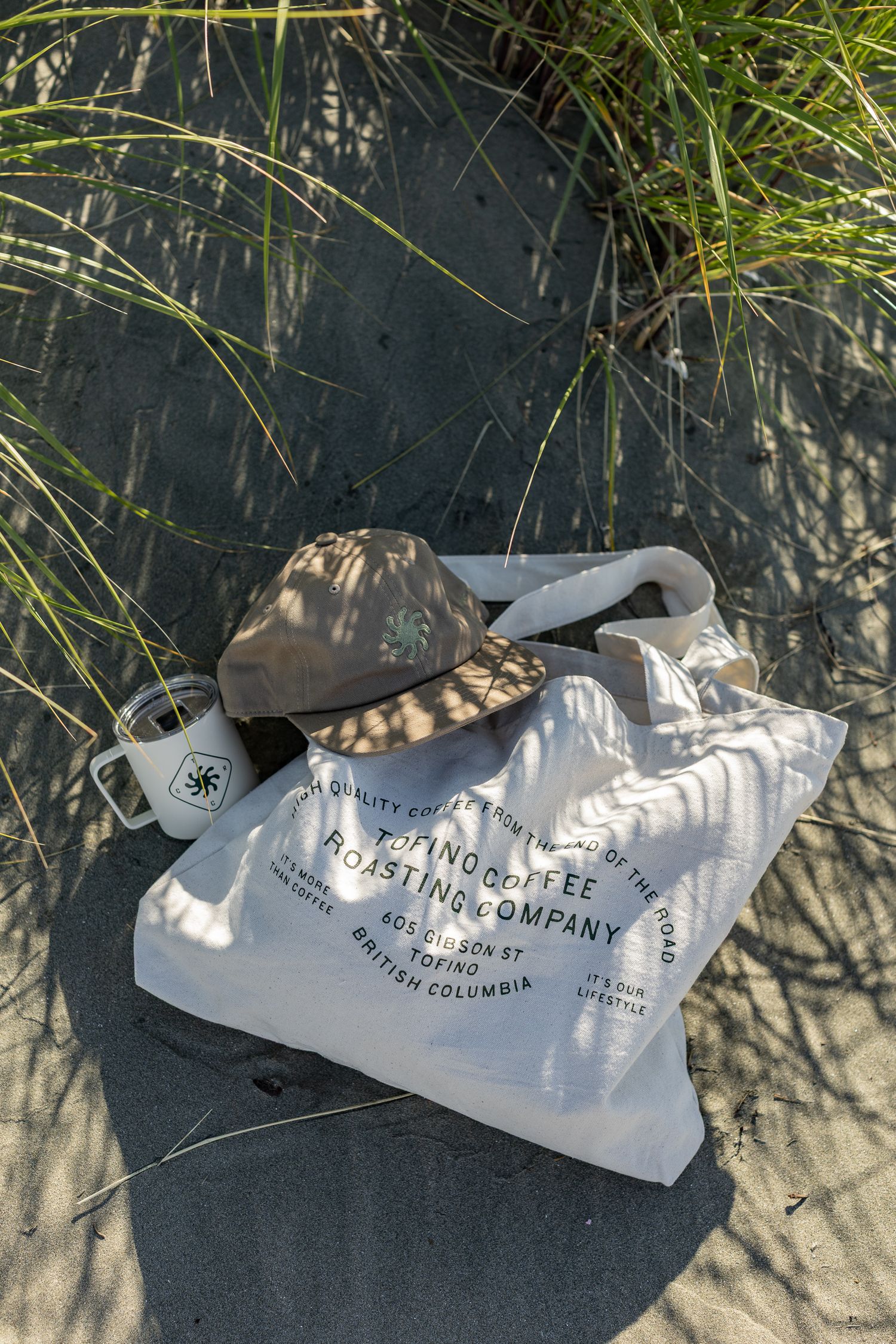 Canvas tote bag from Tofino Coffee Roasting Company with bucket hat on sandy beach dunes.